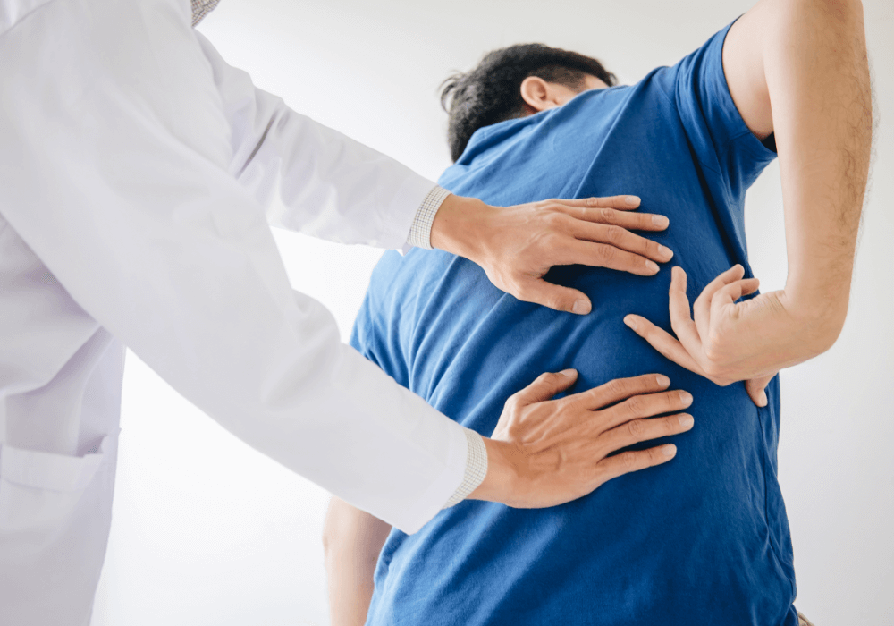 A healthcare professional examines a patient's back, hands positioned on the lower back, assessing for pain or discomfort.