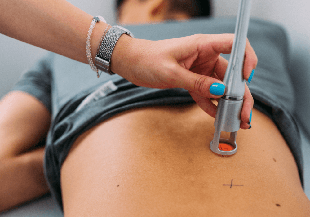 Laser Therapy A healthcare professional uses a device on a patient's lower back, marked with a cross, for treatment or assessment.