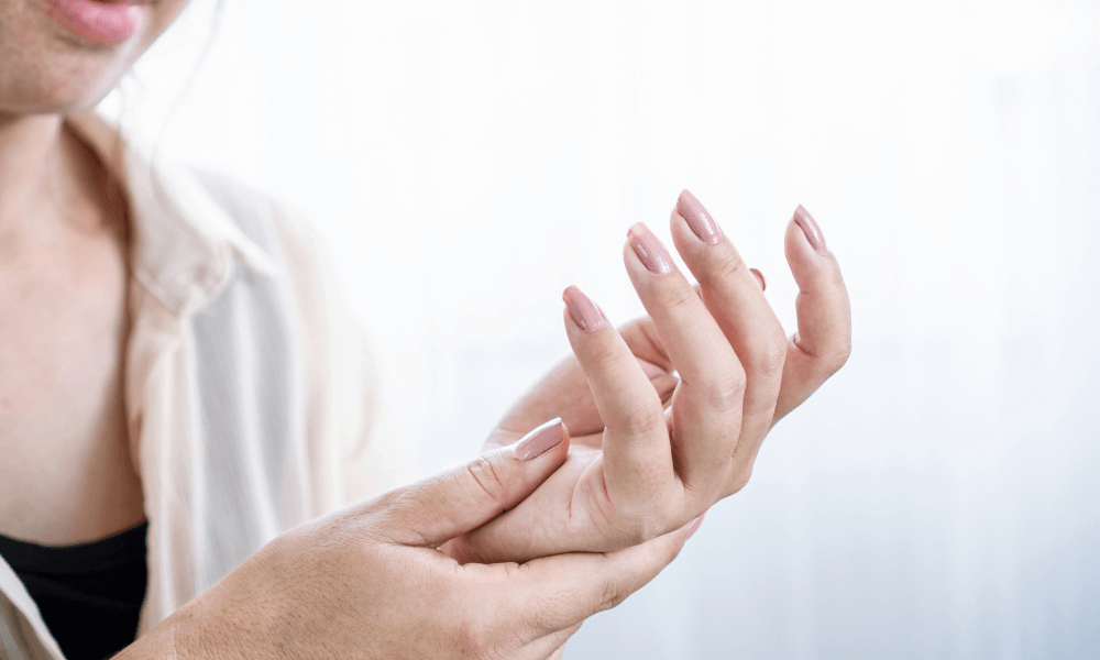 Numbness & Tingling A close-up of a woman gently holding her wrist with one hand, showcasing elegantly manicured nails against a softly blurred background.